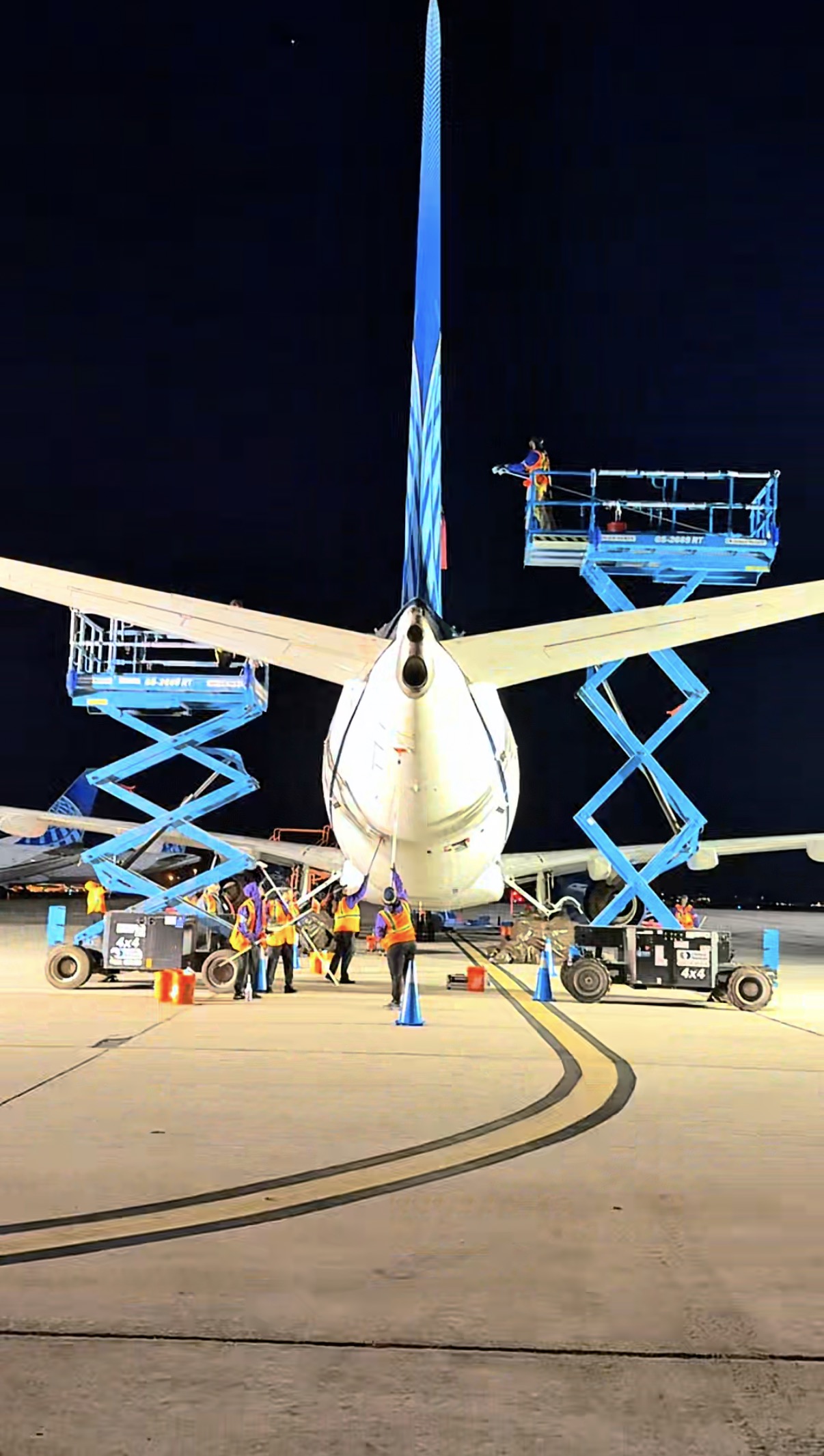 Flightline exterior wash crew working around an aircraft at night with two raised scissor lifts